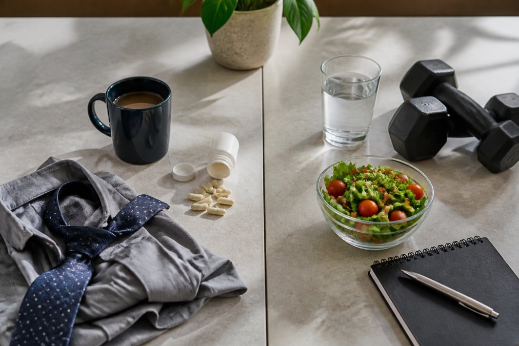 Juxtaposed desk scene: business attire and coffee on the left, a healthy salad, water, dumbbells, and a notebook on the right, suggesting work–fitness balance.]